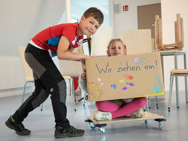 V.l.: Joshua und Frieda von den Heine-Kids rollern gemeinsam die ersten Kartons in den neuen Mehrzweckraum 	Foto: maxpress